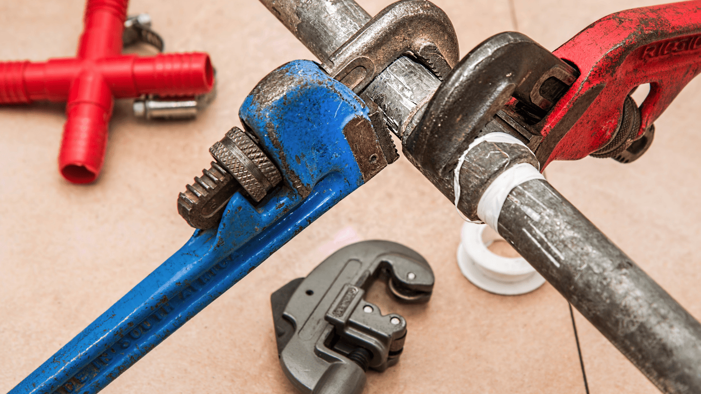 Plumbing tools tightening a metal pipe during repair work.