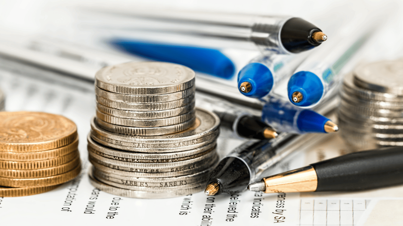 Stacks of silver and gold coins with pens on financial documents representing money management and budgeting