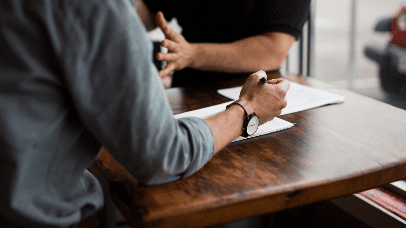 Two people sitting at a wooden table discussing documents during a meeting.