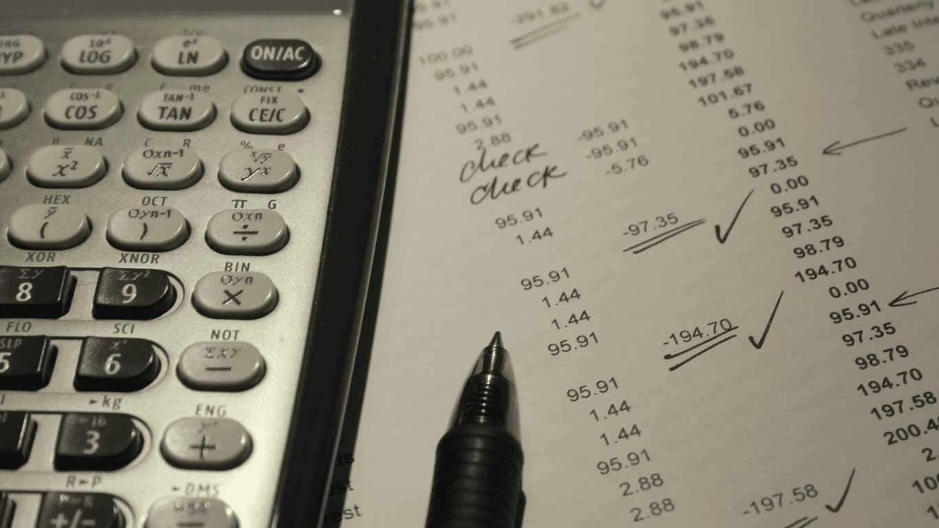 Close-up of a calculator, pen, and financial report with handwritten notes and check marks.