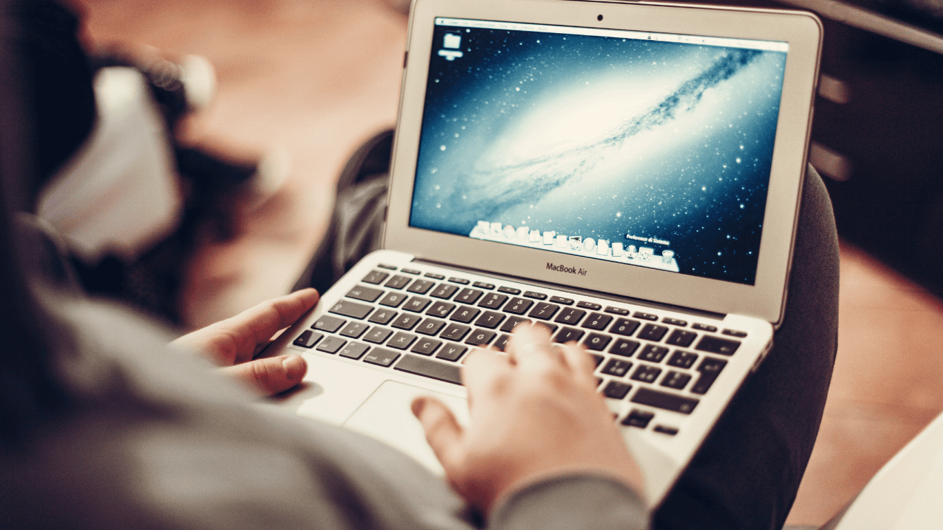 Person using a MacBook Air laptop with the screen displaying a desktop background.