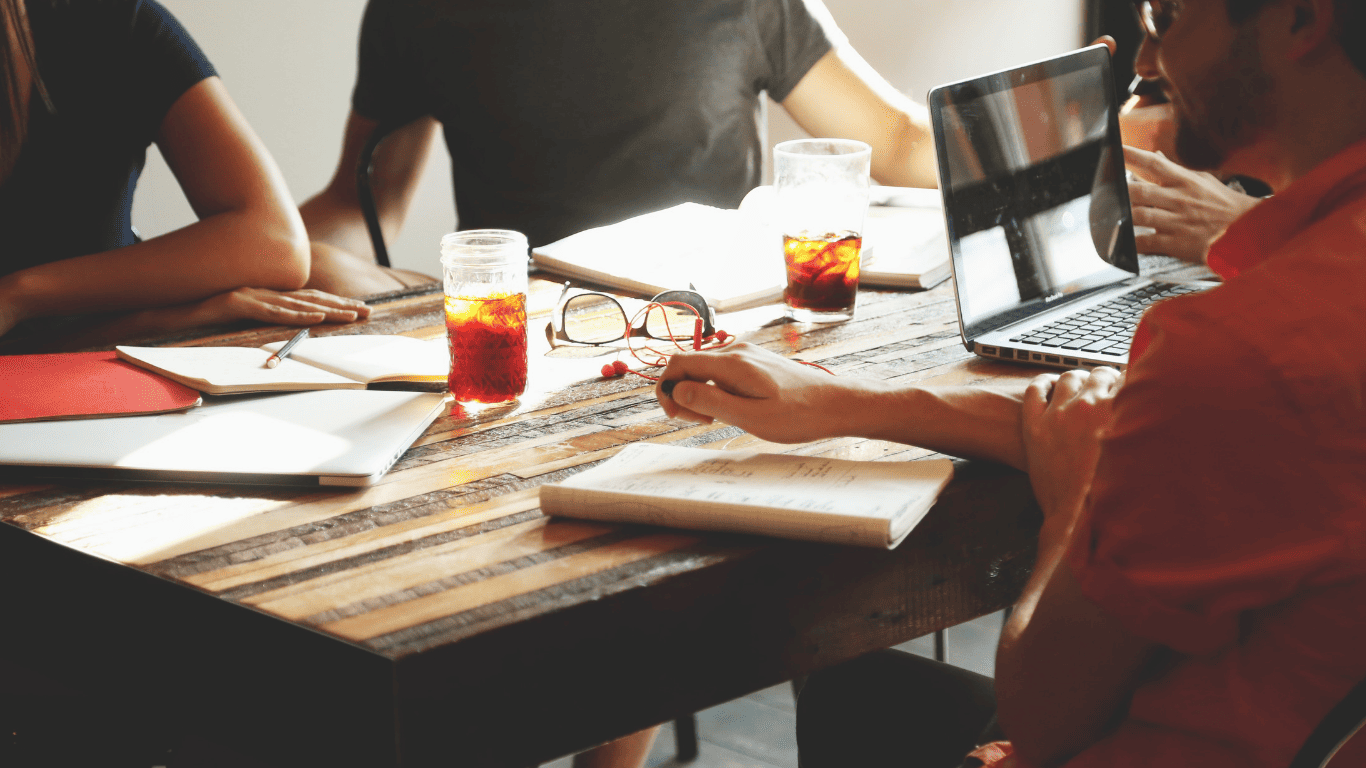 Group of people having a casual meeting with laptops, notebooks, and drinks on the table.
