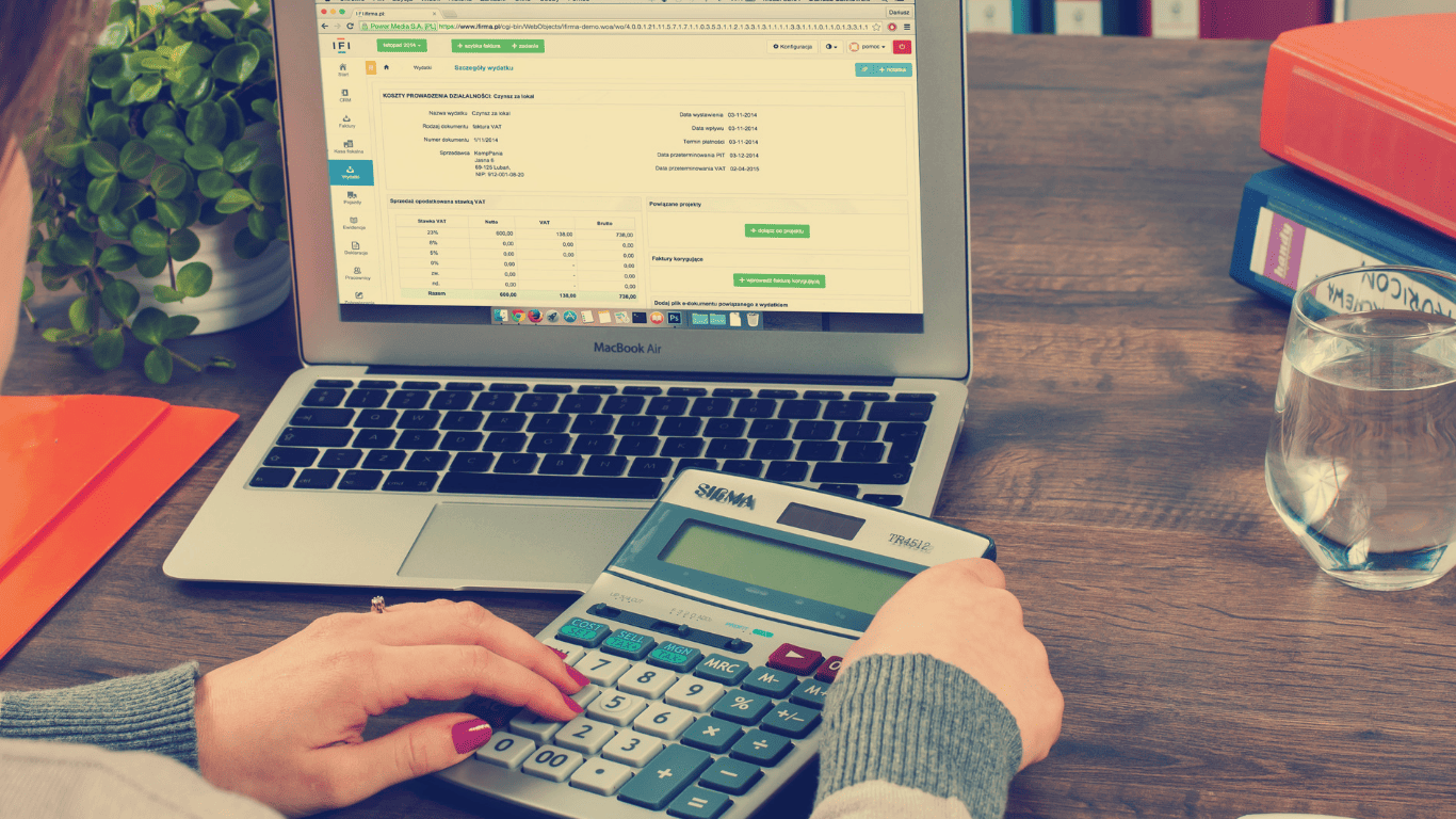 Woman using a calculator while reviewing financial data on a laptop at a desk.