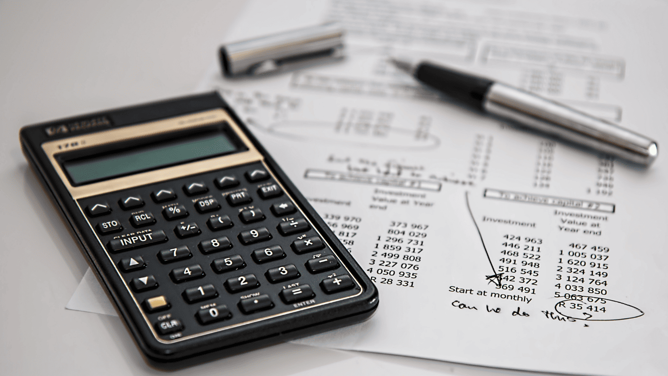 Close-up of a calculator, pen, and financial documents with investment figures and notes.
