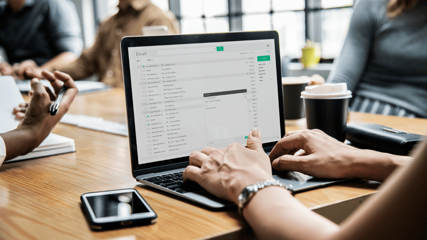 Person managing emails on a laptop during a business meeting with colleagues