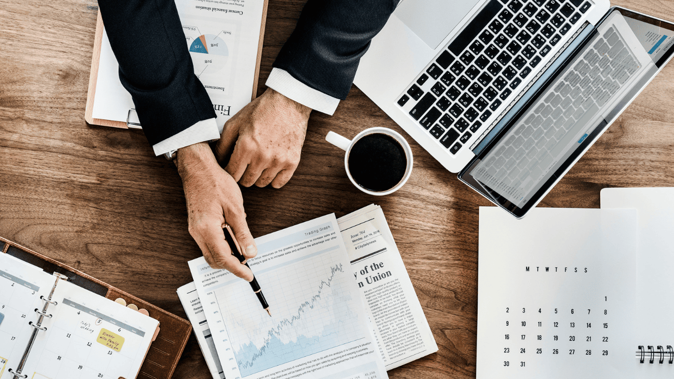 Business professional analyzing financial charts and data with laptop, documents, and calendar on desk.