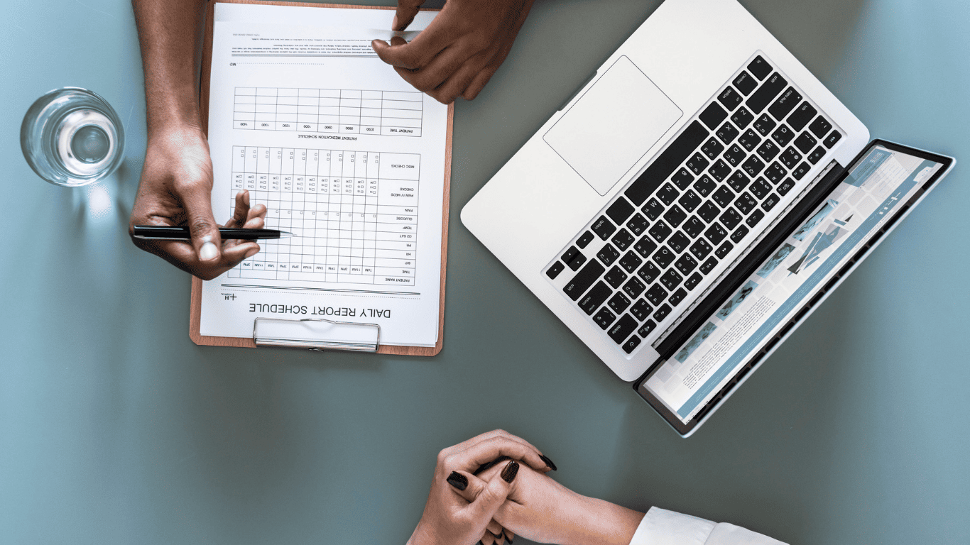 Business meeting with a daily report schedule on a clipboard and a laptop on the table.