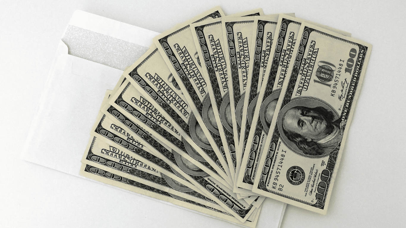 Stack of hundred-dollar bills fanned out beside a white envelope.