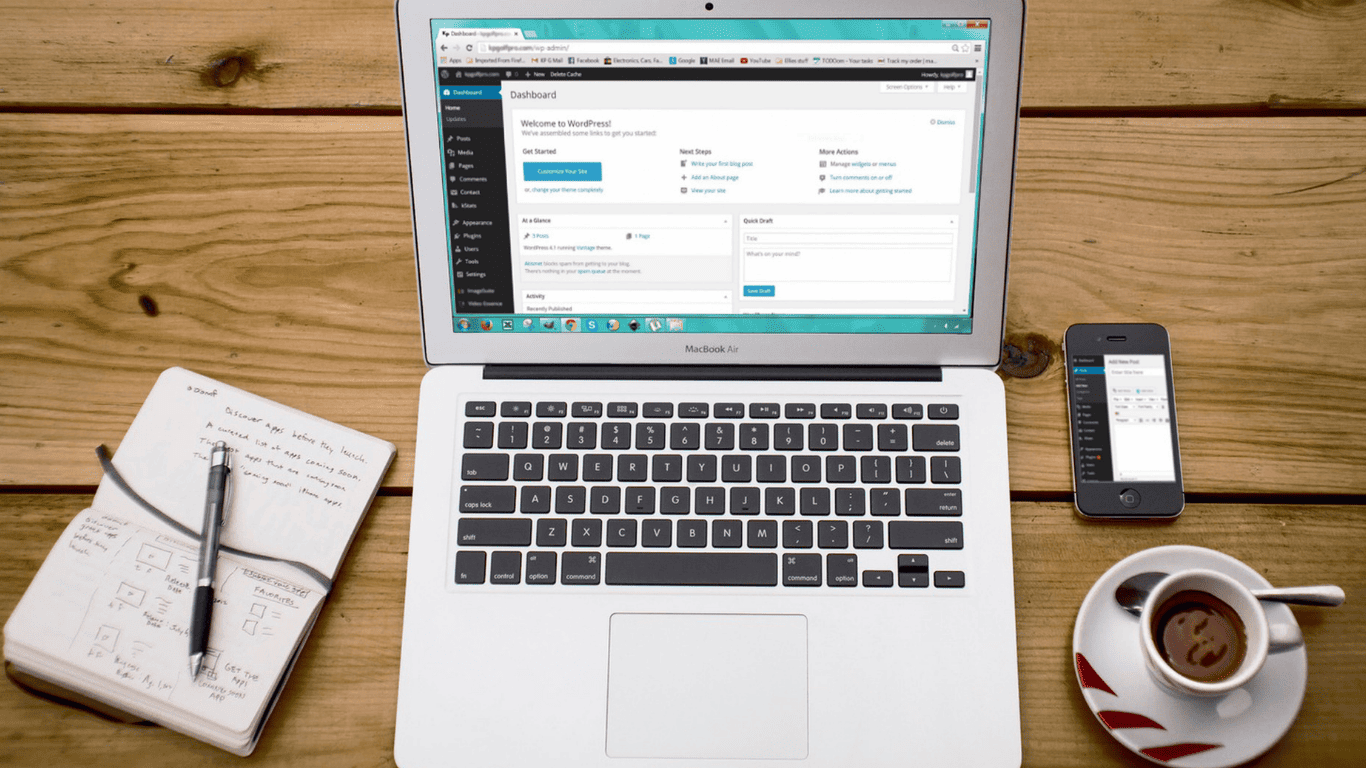 Laptop displaying WordPress dashboard with notebook, smartphone, and coffee cup on a wooden desk
