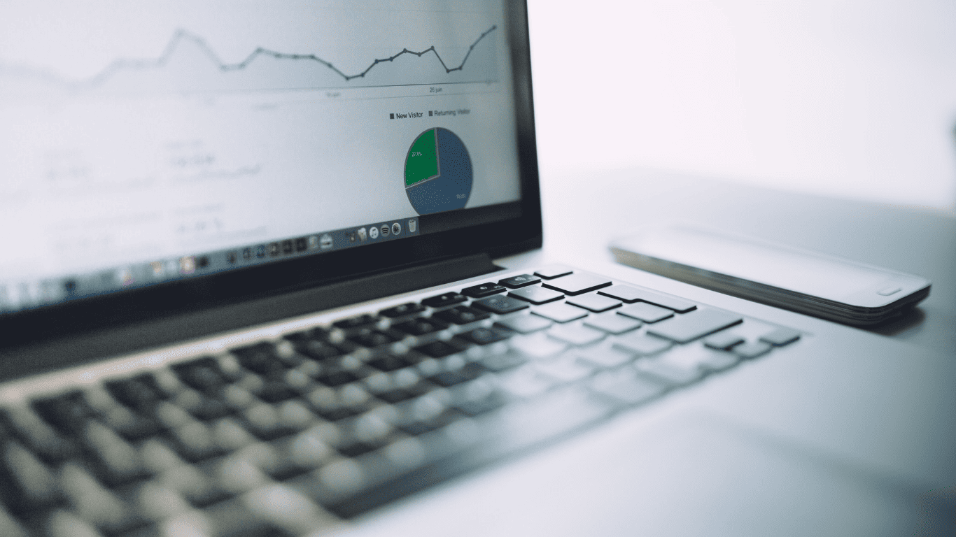 Close-up of a laptop screen displaying analytics graphs and pie chart, with a smartphone placed nearby.