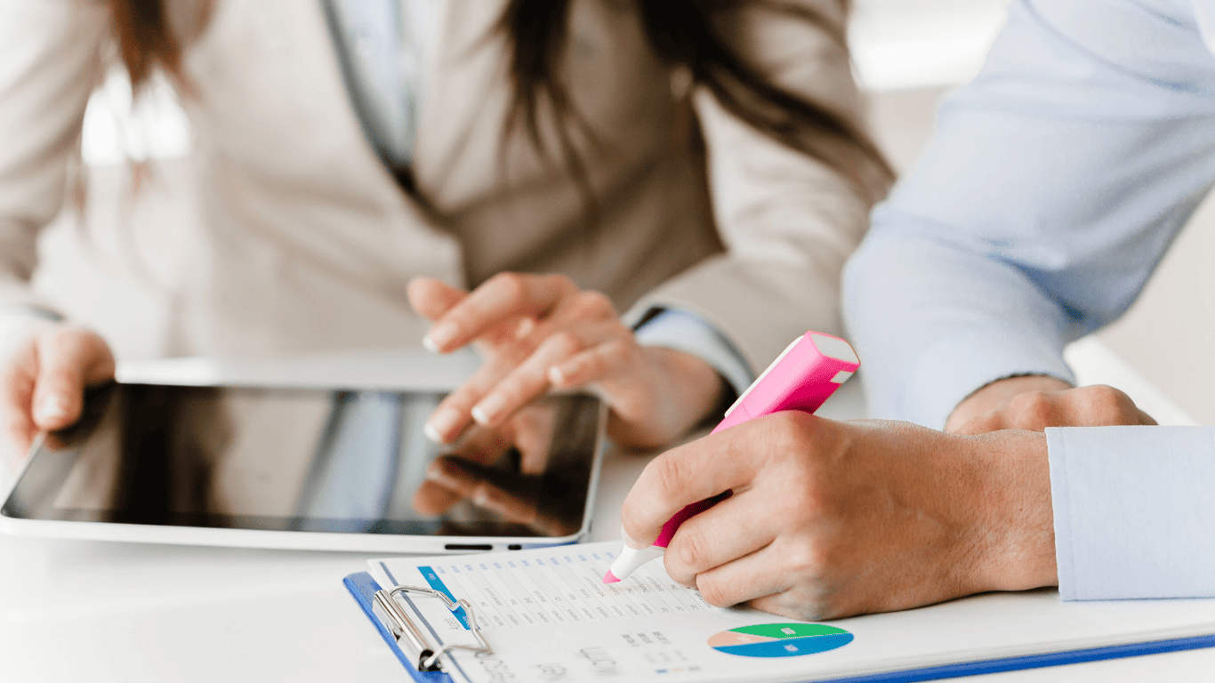 Close-up of professionals reviewing charts, with one person highlighting data and another using a tablet.