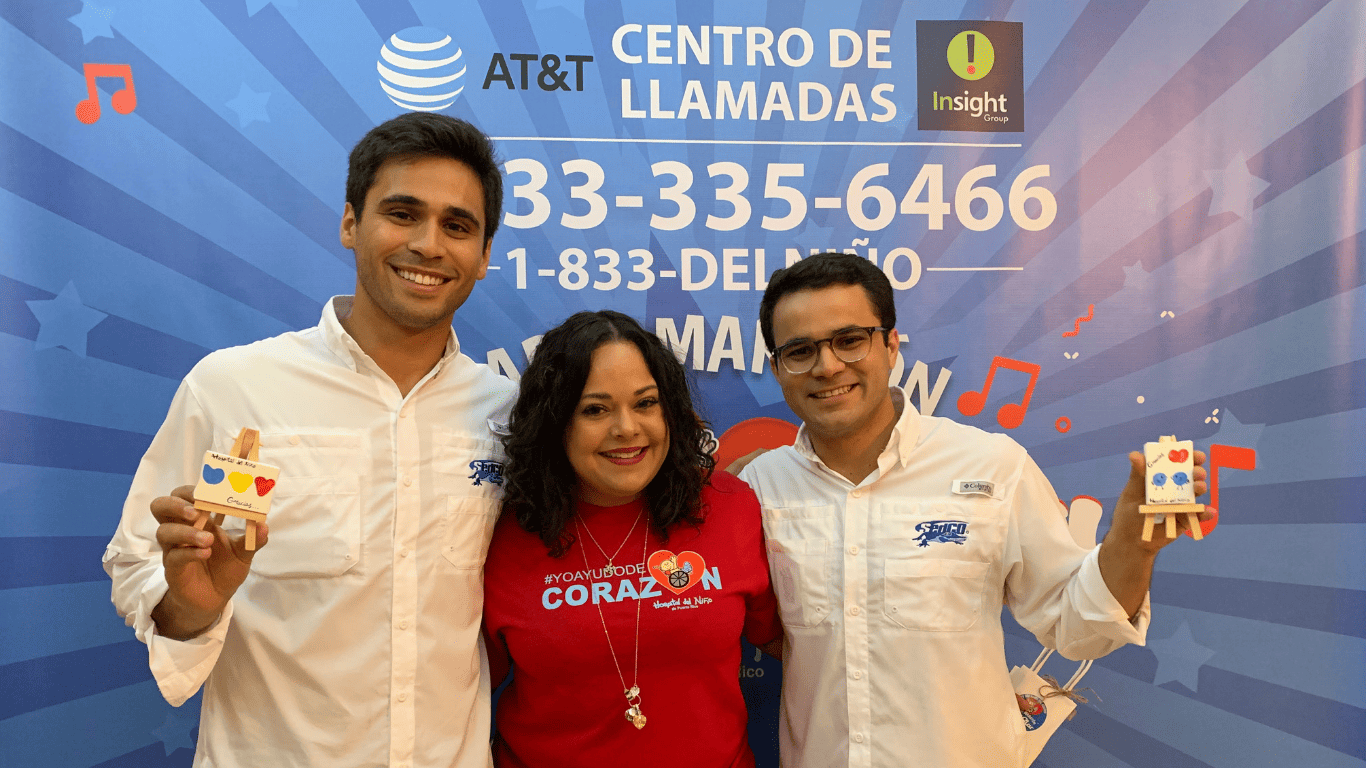 Three people smiling at a community event with a call center support banner in the background.