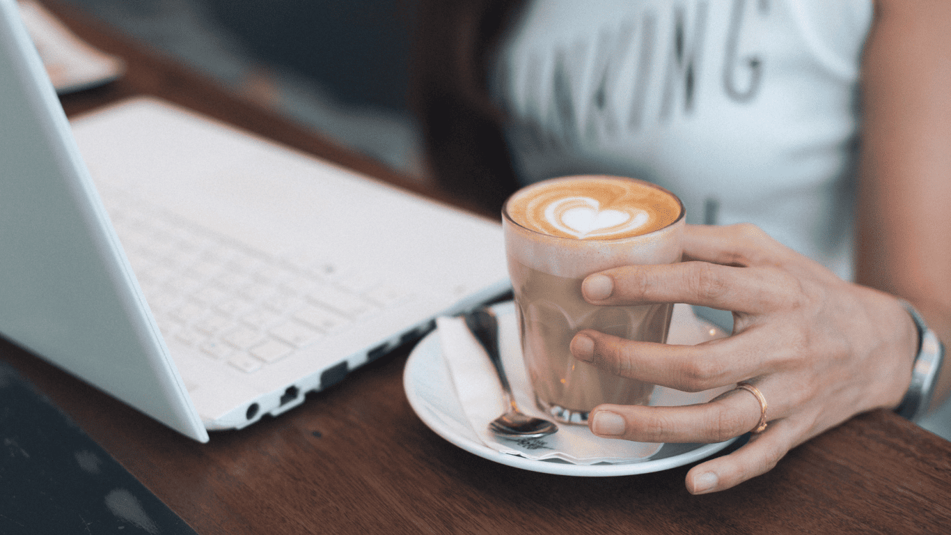 Person holding a cup of coffee with latte art while working on a laptop.