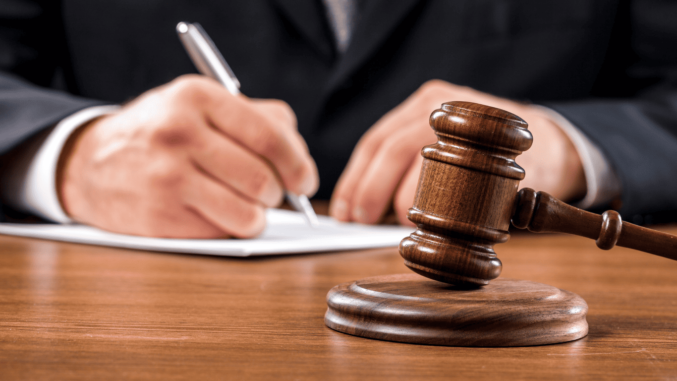 Close-up of a judge’s gavel with a person signing legal documents in the background.