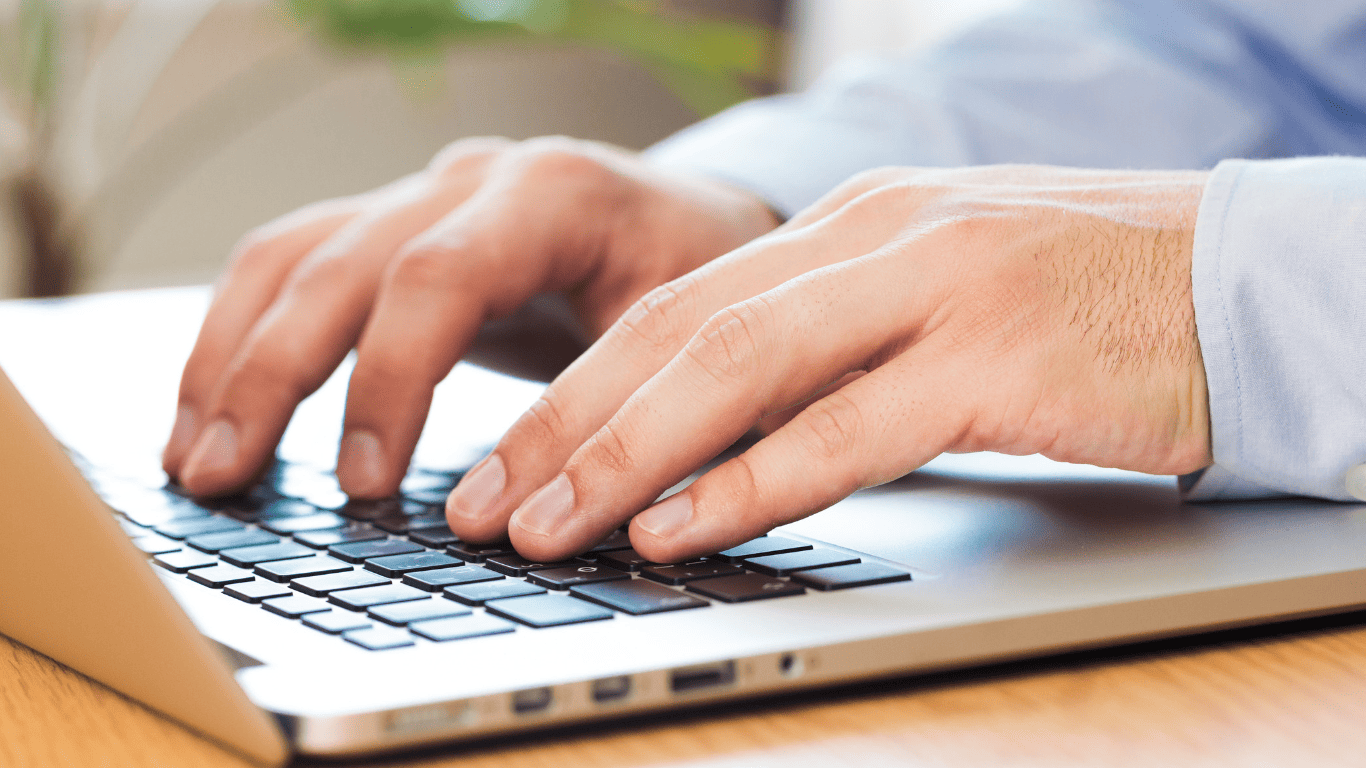 Close-up of hands typing on a laptop keyboard in a bright office setting