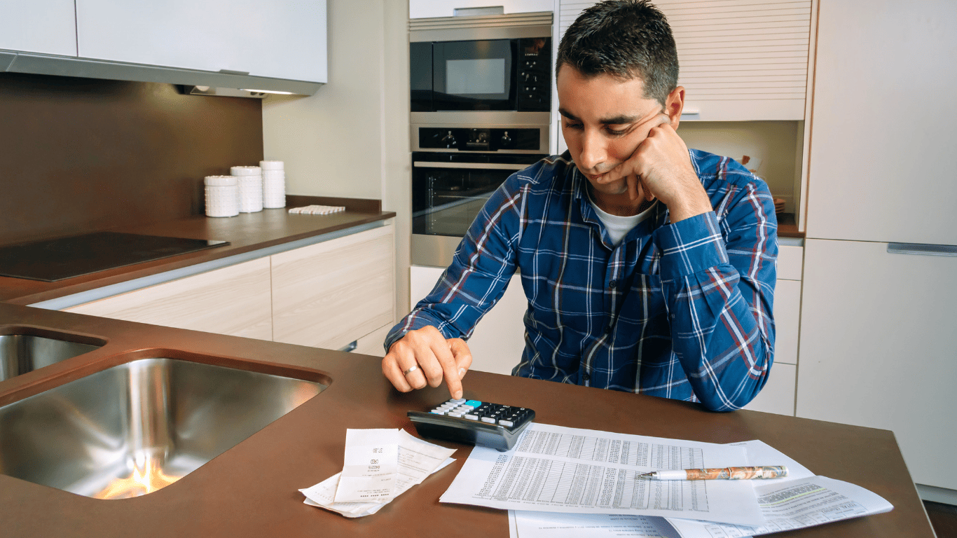Man sitting at a kitchen table using a calculator to review receipts and bills.