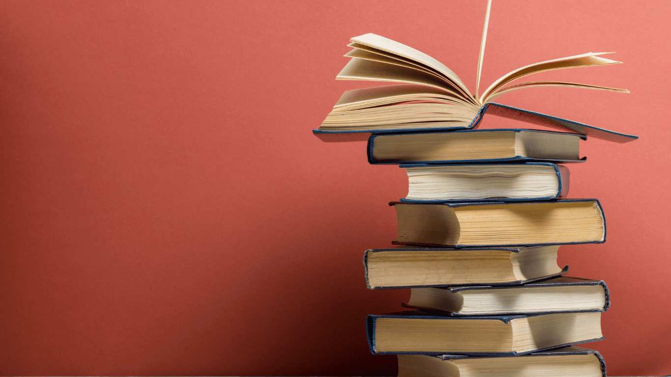 Stack of old books with an open book on top against a red background, symbolizing knowledge and learning