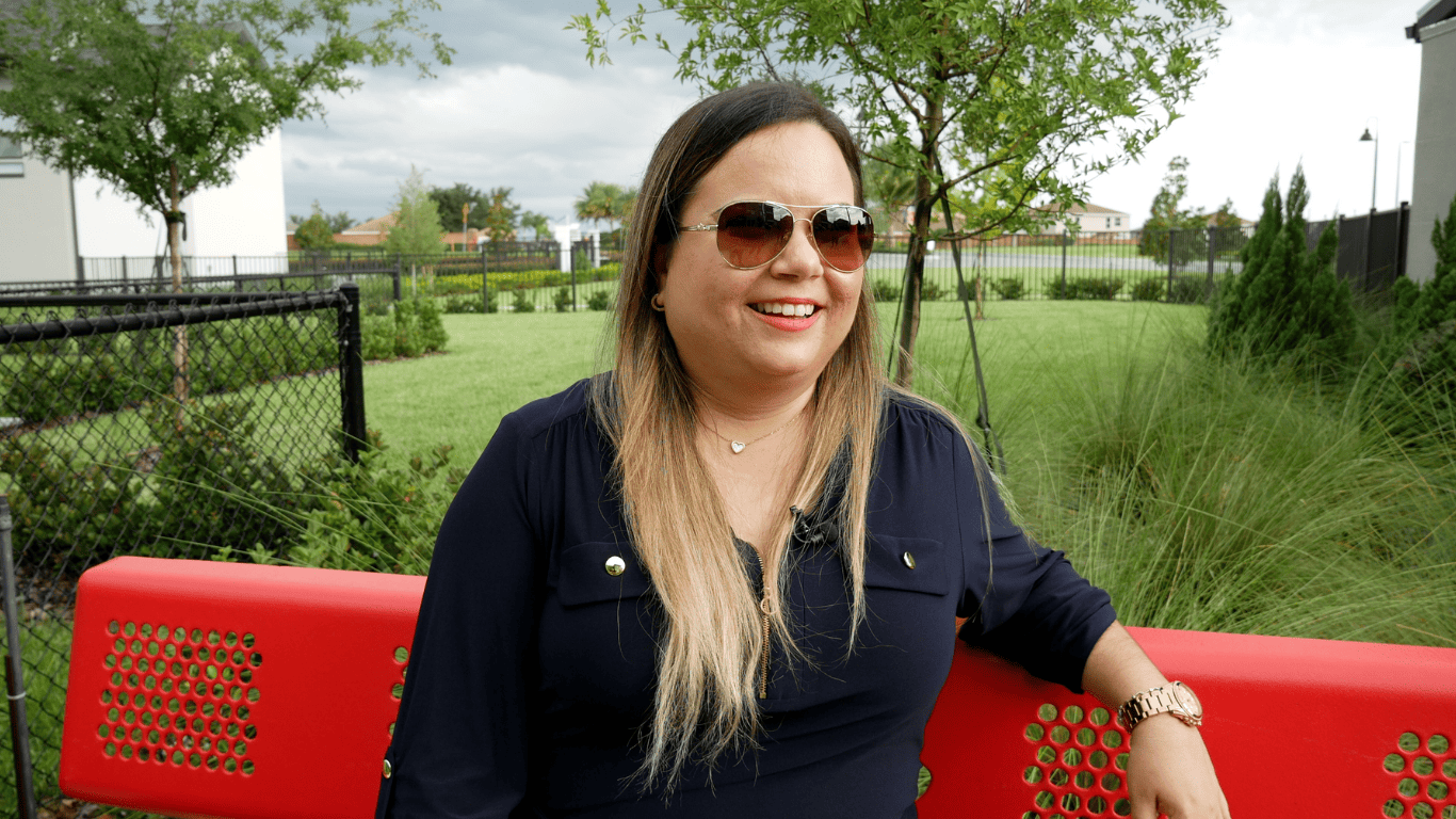 Smiling woman wearing sunglasses sitting on a red bench in a park.