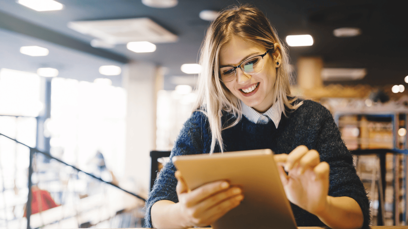 Smiling woman using a tablet while sitting in a coffee shop.